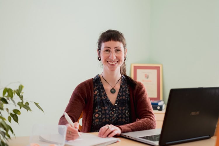 Entspannte Frau arbeitet im Homeoffice mit Laptop und Notizbuch.