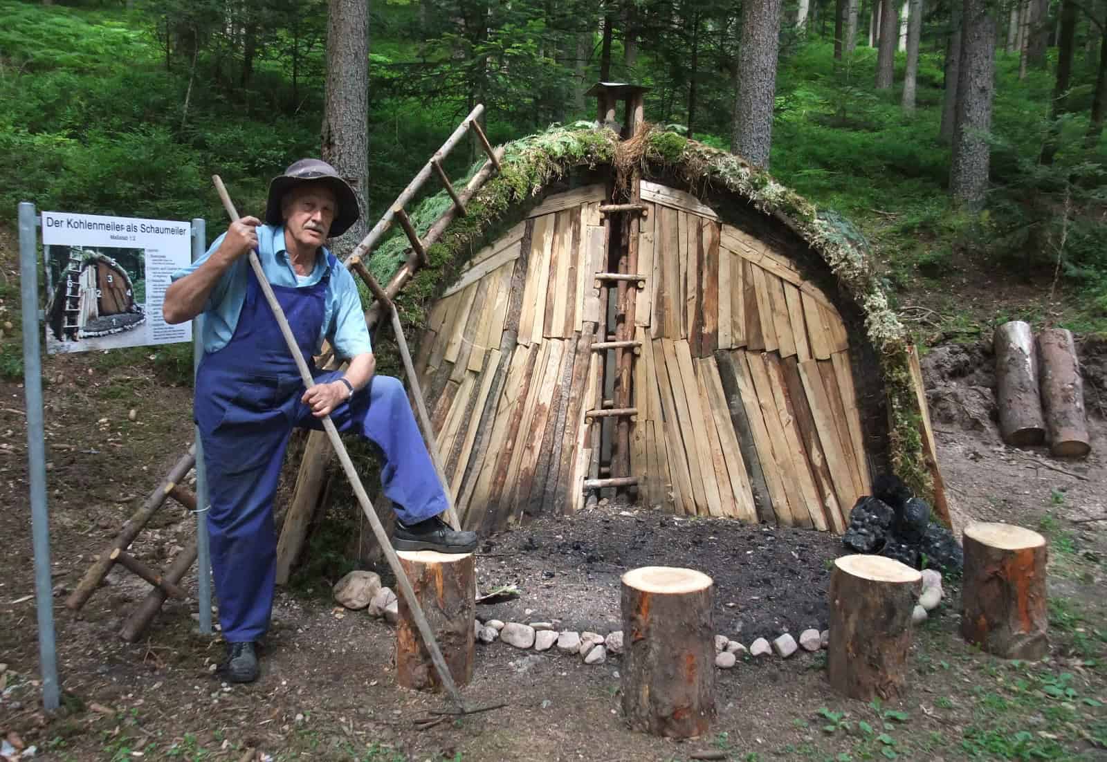 Holzofen im Wald, historische Bauweise, Waldarbeiter zeigt traditionelles Handwerk, nachhaltige Holzbearbeitung, Natur und Handwerkskunst, authentische Umwelt.