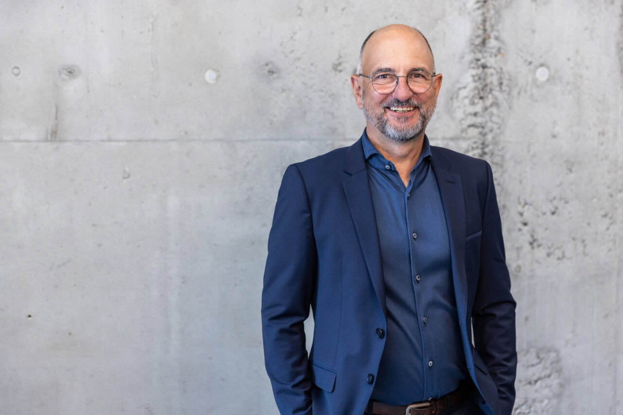 Moderner Mann in Geschäftsanzug vor Betonwand, professionelles Business-Image, Selbstvertrauen und Erfolg.