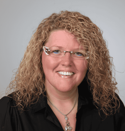 Authentische weibliche Coach-Person mit lockigem Haar, Smiley und Brille, professionell und vertrauenswürdig.